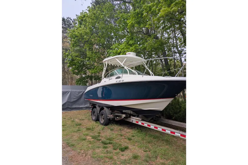 Slide: The Image of 2016 Wellcraft 252 Coastal boat on trailer, surrounded by lush green trees. - 7