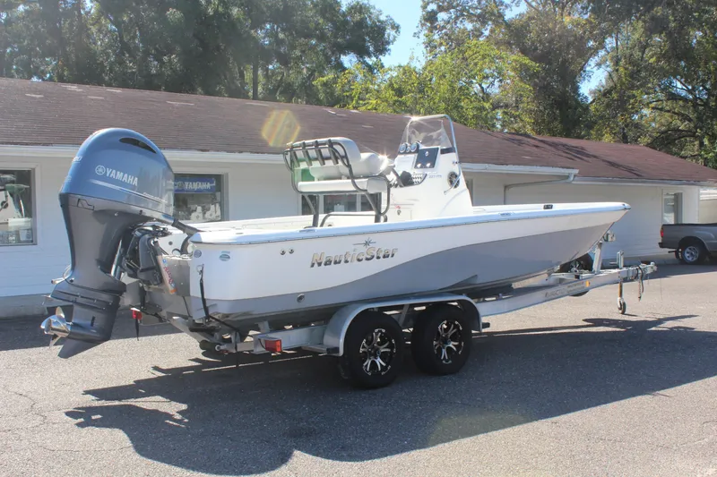 Slide: The Image of 2022 NauticStar 227 Bay boat on trailer with Yamaha outboard motor, parked outdoors. - 13