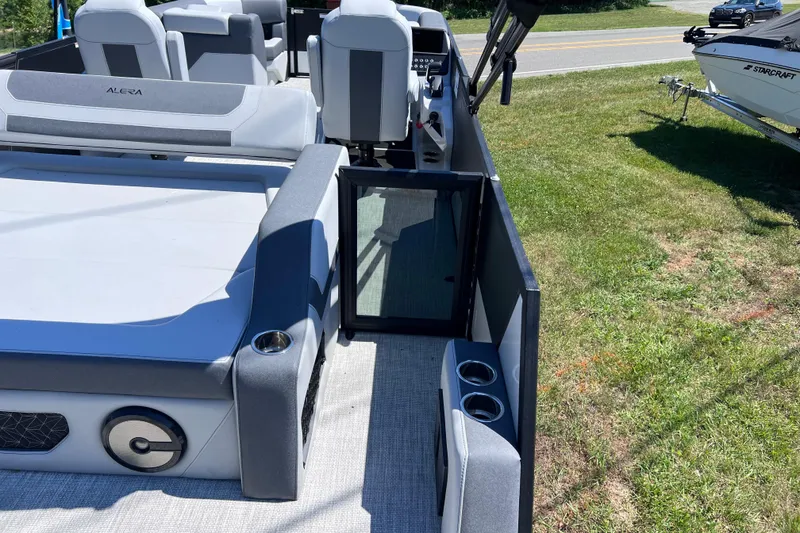 Slide: The Image of Alera M23L 2026 boat interior with seating and cup holders, parked on grass. - 14