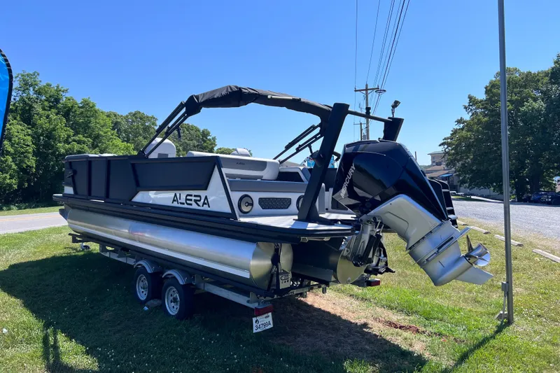Slide: The Image of 2026 Alera M23L pontoon boat on trailer, parked on grass under clear blue sky. - 3