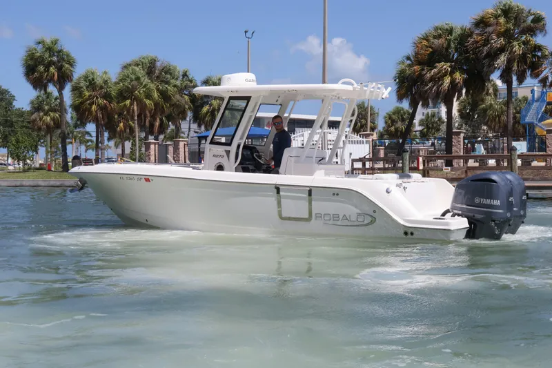 Slide: The Image of 2020 Robalo R272 Center Console boat cruising on water with palm trees in background. - 2
