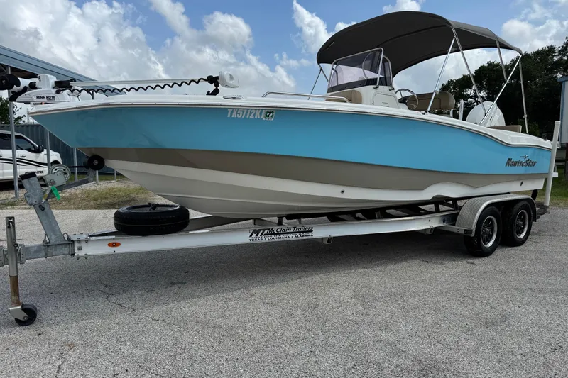 The Image of 2020 NauticStar 231 Hybrid boat on trailer, blue and white, parked outdoors. - 1