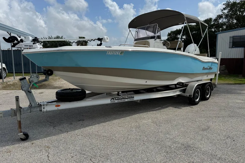 Slide: The Image of 2020 NauticStar 231 Hybrid boat on trailer, blue and white, parked outdoors. - 2