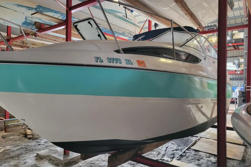 Slide: The Image of 2003 Bayliner 245 boat in storage, featuring a white and teal exterior. - 2