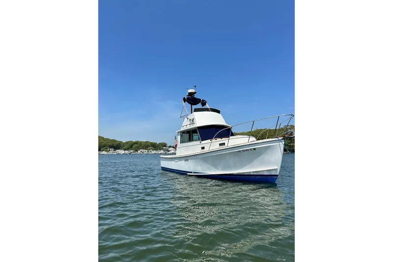 The Image of 1987 Cape Dory 28 Flybridge boat on calm water under clear blue sky. - 0
