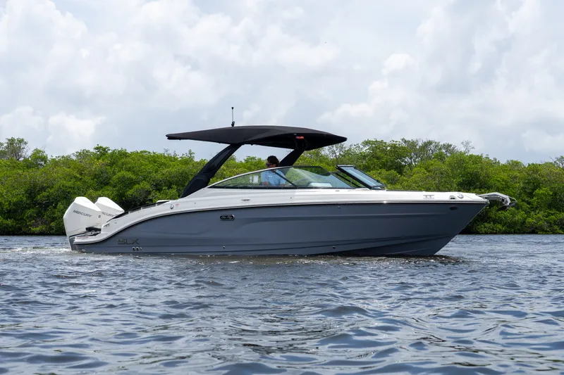 Slide: The Image of A sleek 2027 Sea Ray SLX 280 Outboard boat cruising on calm water with a green shoreline backdrop. - 35