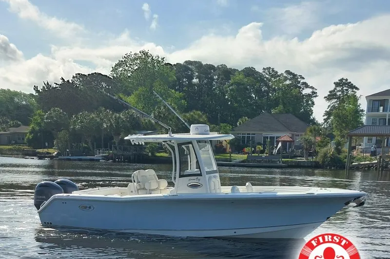 The Image of 2019 Sea Hunt Gamefish 27 boat on calm water, surrounded by lush greenery and houses. - 10