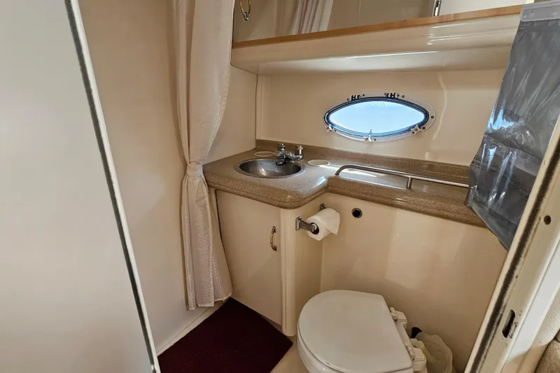 Slide: The Image of Compact bathroom in a 2000 Larson Cabrio 330 boat, featuring sink, toilet, and porthole window. - 23