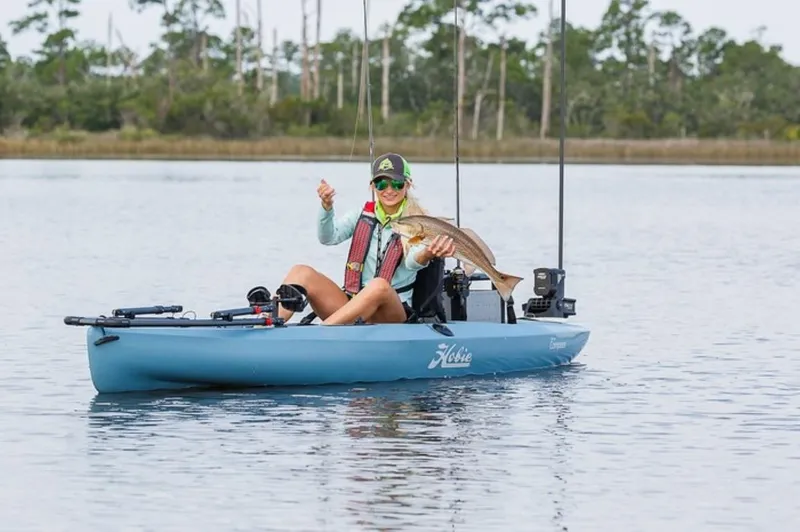 The Image of Person fishing on a 2023 Hobie Compass kayak, holding a fish in a serene lake. - 0