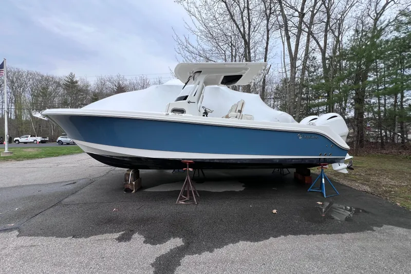 The Image of 2022 Edgewater 262CC boat on stands, blue hull, parked outdoors near trees. - 0