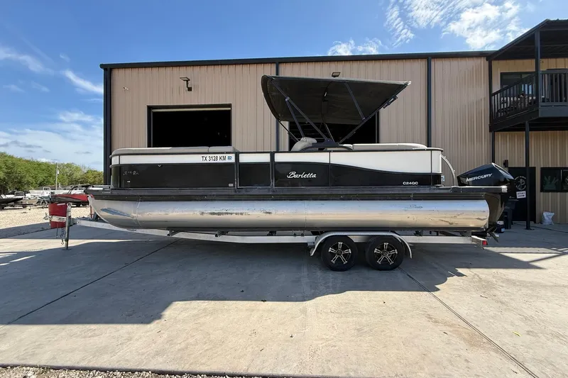 The Image of 2020 Barletta C24QC pontoon boat on trailer, parked outside a building under a clear sky. - 1