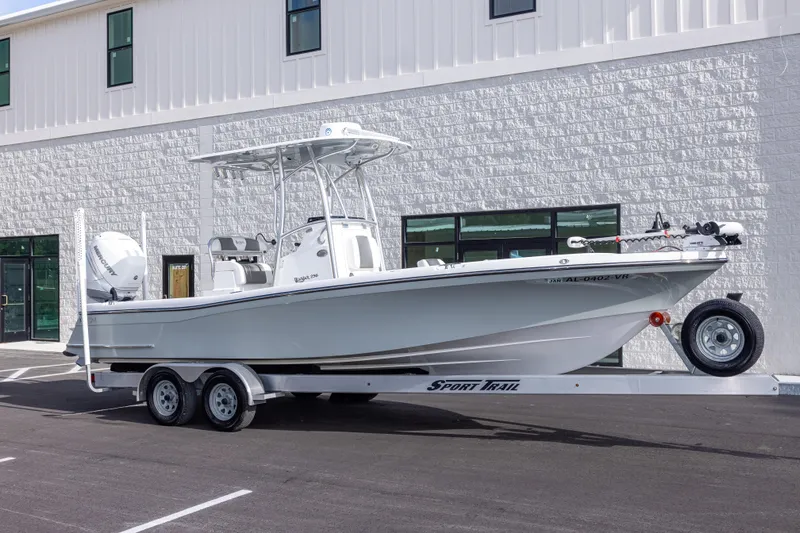 Slide: The Image of 2022 BlackJack 256 Coastal boat on trailer, parked outside a modern building. - 2