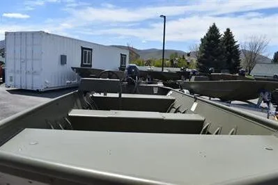 Slide: The Image of 2025 Lowe L1648M Jon boat displayed outdoors with trees and container in background. - 10