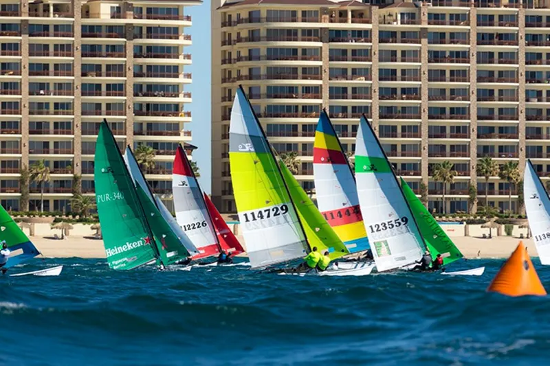 Slide: The Image of Colorful Hobie Cat H16 sailboats racing near beachfront buildings, 2023 model. - 9