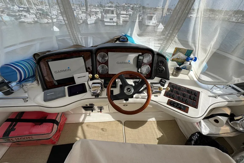 Slide: The Image of 2006 Sea Ray 44 Sedan Bridge helm with Garmin navigation, wooden steering wheel, and marina view. - 33