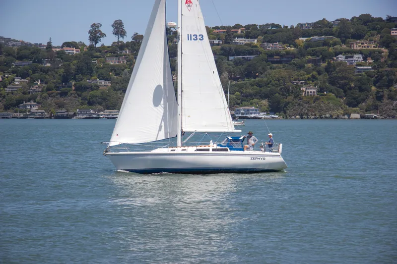 Slide: The Image of Sailboat Catalina 36, 1991 model, cruising on a scenic lake with lush hillside backdrop. - 3