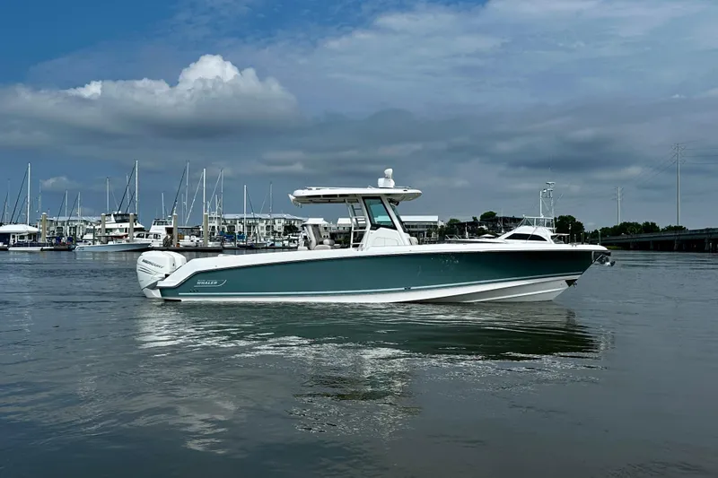 Slide: The Image of 2019 Boston Whaler 330 Outrage boat on calm water near marina, under cloudy sky. - 2