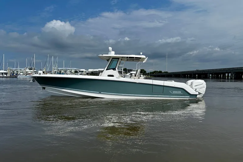 Slide: The Image of 2019 Boston Whaler 330 Outrage boat on calm water, with marina and cloudy sky backdrop. - 5