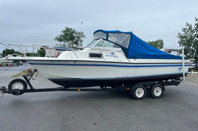 Slide: The Image of 1995 Celebrity 2500 Fish Hawk boat on trailer with blue cover, parked outdoors. - 3