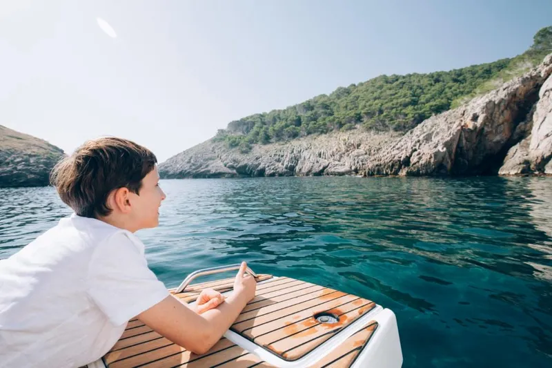 Slide: The Image of Boy enjoying scenic view from Beneteau Flyer 10 boat, 2024 model, near rocky coastline. - 53