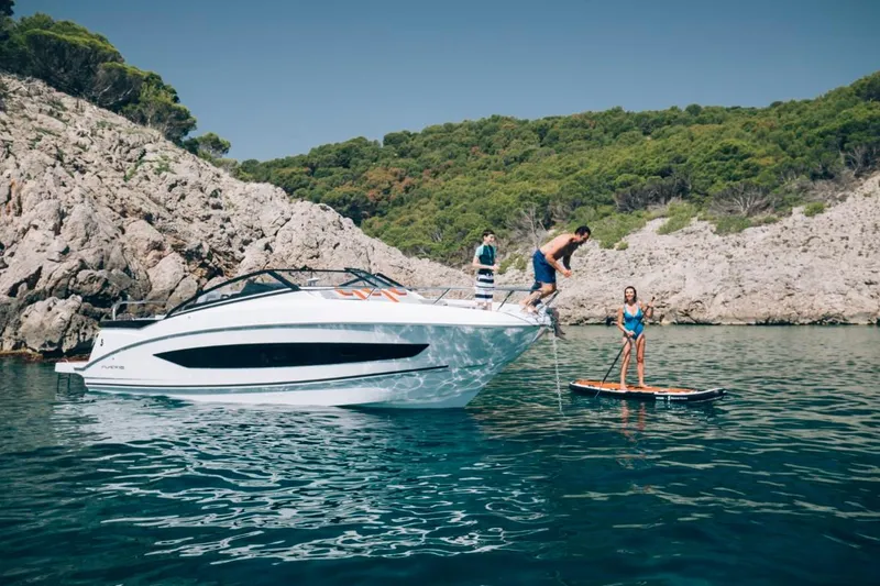 Slide: The Image of 2024 Beneteau Flyer 10 boat with people enjoying water activities near rocky shore. - 8