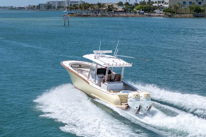 Slide: The Image of 2020 Mag Bay 33 CC boat cruising on clear blue water near a coastal city. - 20