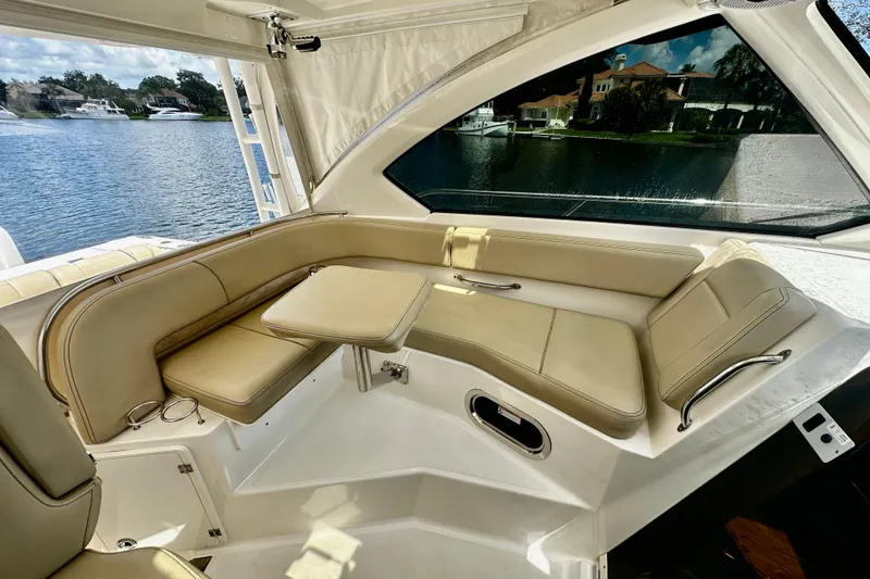Slide: The Image of 2019 Pursuit OS 325 Offshore boat interior with beige seating and table, overlooking water. - 12