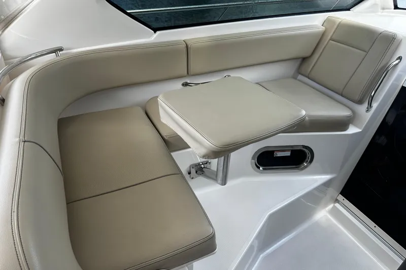 Slide: The Image of 2019 Pursuit OS 325 Offshore boat interior seating with beige cushions and compact table. - 13