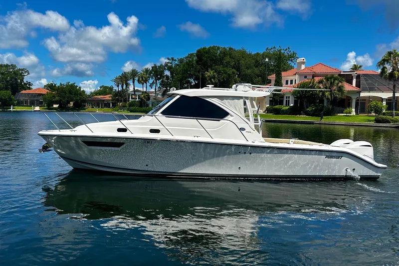 Slide: The Image of 2019 Pursuit OS 325 Offshore boat on a serene lake with luxury homes in the background. - 2