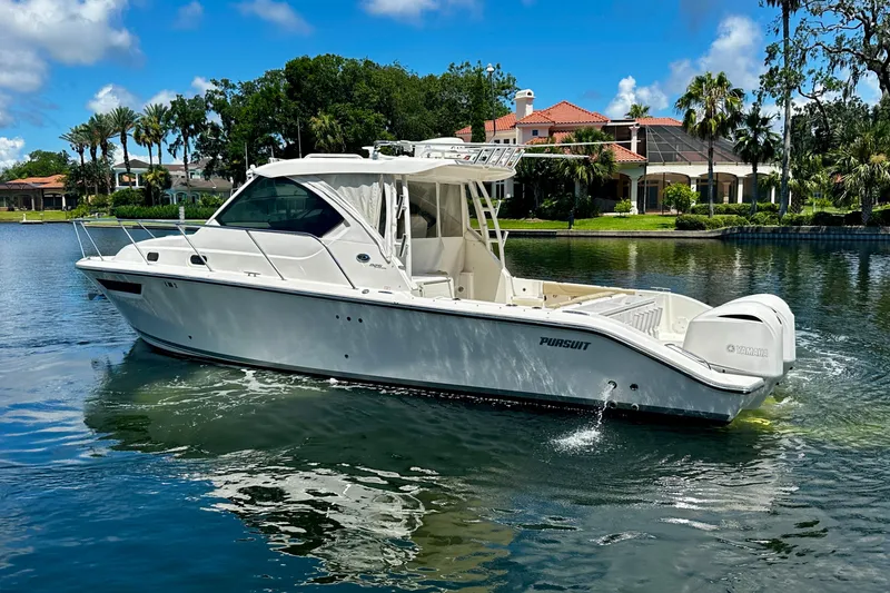 Slide: The Image of 2019 Pursuit OS 325 Offshore boat cruising on a serene lake with lush greenery. - 3