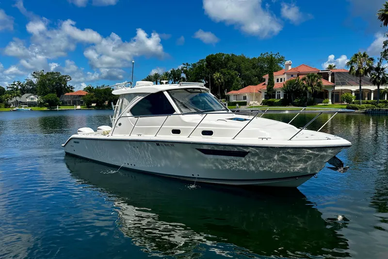 Slide: The Image of 2019 Pursuit OS 325 Offshore boat on a serene lake with luxury homes in the background. - 5