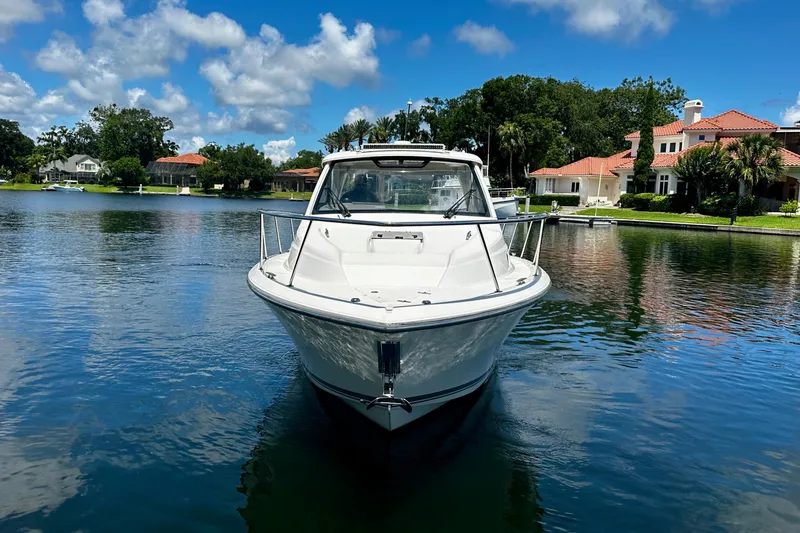 Slide: The Image of 2019 Pursuit OS 325 Offshore boat on a serene lake with luxury homes in the background. - 6