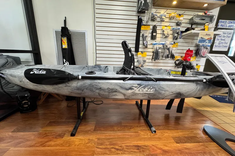 The Image of 2024 Hobie Mirage Compass kayak displayed in a store with accessories on shelves. - 0