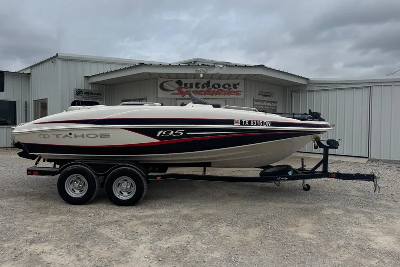 The Image of 2015 Tahoe 195 boat on trailer outside dealership under cloudy sky. - 1