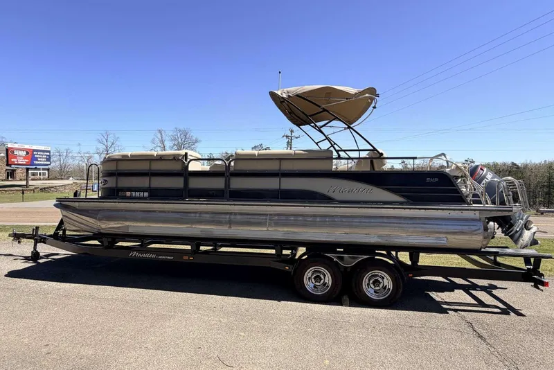 The Image of 2017 Manitou 25 SES BENCH pontoon boat on trailer, parked outdoors under clear blue sky. - 0