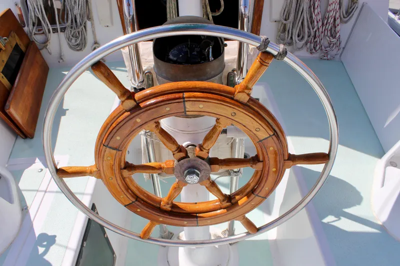 Slide: The Image of Wooden steering wheel on a 1975 Downeast 38 sailboat, surrounded by nautical ropes. - 23