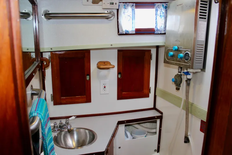 Slide: The Image of 1975 Downeast 38 boat bathroom with wooden cabinets, stainless steel sink, and compact water heater. - 58