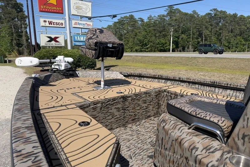 Slide: The Image of 2026 Xpress H22B Bay boat with camouflage design, parked near dealership signs. - 9