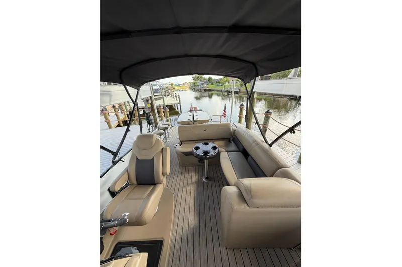 Slide: The Image of 2022 Starcraft CX 25 DL BAR boat interior with seating and table, docked by a calm waterway. - 10