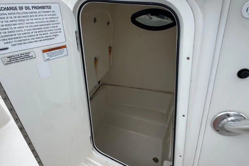 Slide: The Image of 2023 Sailfish 242 CC boat storage compartment with open door and warning labels. - 35