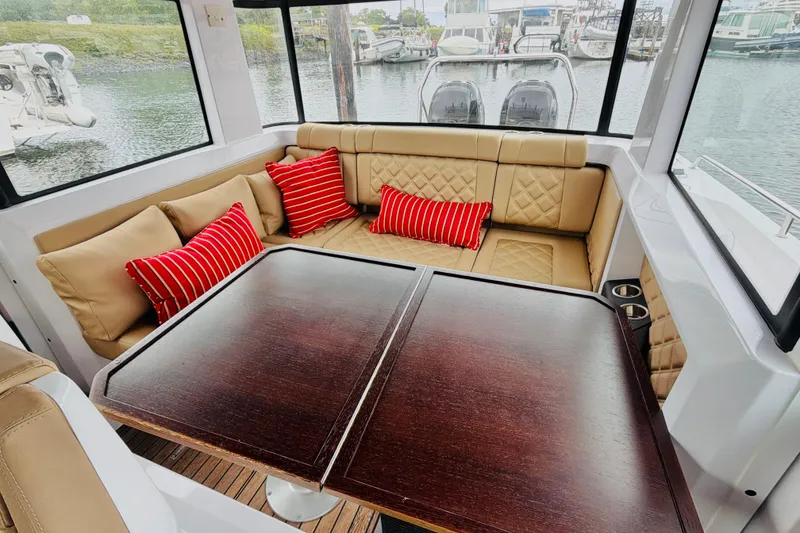Slide: The Image of 2020 Axopar 37 XC Cross Cabin interior with beige seating, red striped pillows, and wooden table. - 26