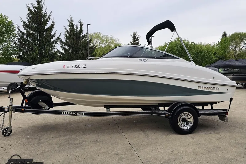Slide: The Image of 2020 Rinker 19QX BR boat on trailer, parked outdoors with trees in background. - 29