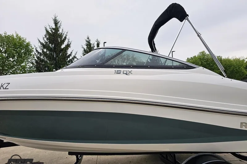 Slide: The Image of 2020 Rinker 19QX BR boat with canopy, parked on trailer, surrounded by trees. - 30