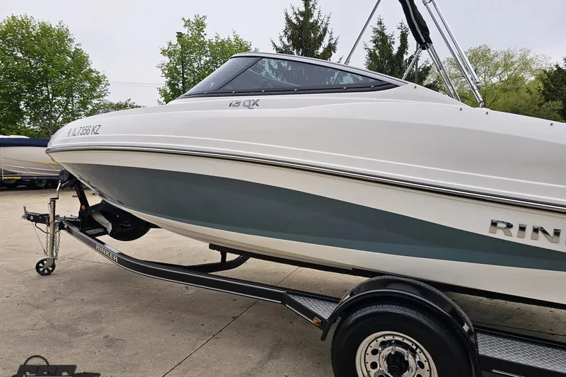 Slide: The Image of 2020 Rinker 19QX BR boat on trailer, parked outdoors with trees in background. - 33