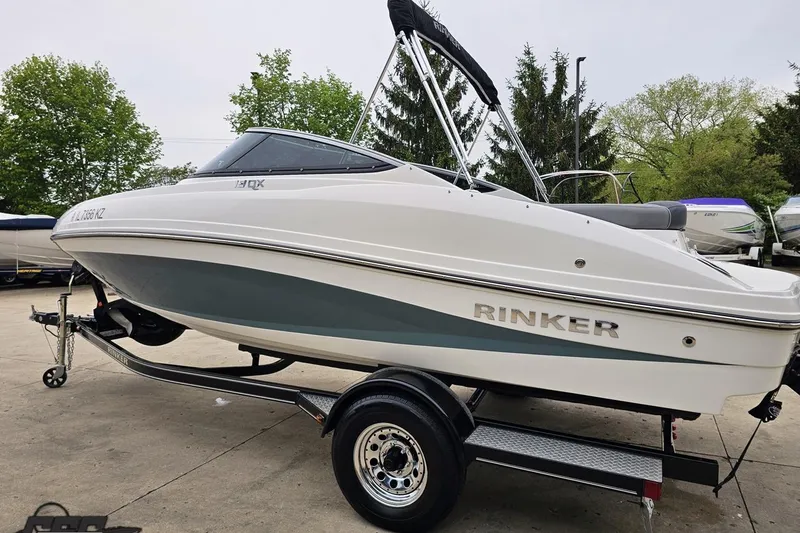 Slide: The Image of 2020 Rinker 19QX BR boat on trailer, white and blue design, parked outdoors. - 34
