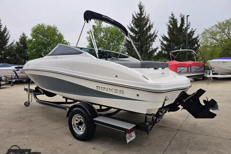 Slide: The Image of 2020 Rinker 19QX BR boat on trailer, parked outdoors with trees in background. - 35