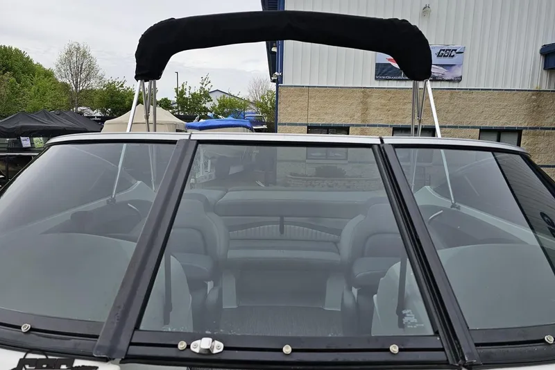 Slide: The Image of 2020 Rinker 19QX BR boat with black bimini top, parked outdoors near a building. - 79