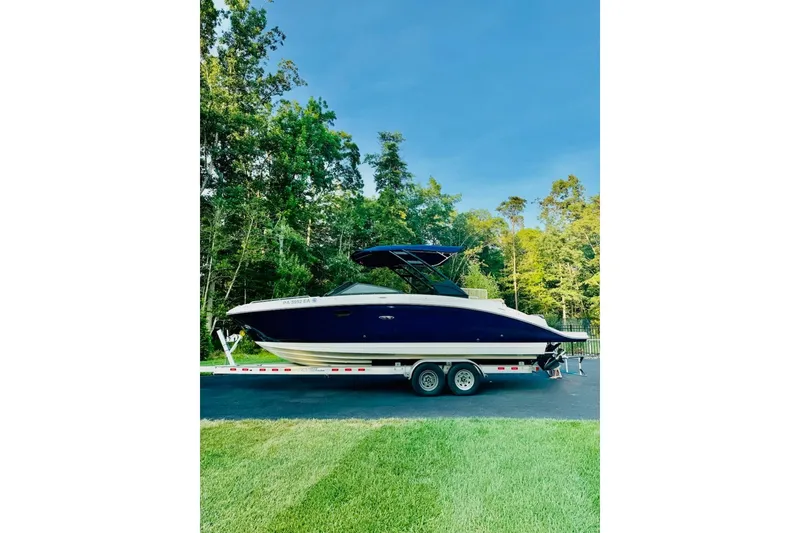 The Image of 2021 Sea Ray SDX 270 boat on trailer, parked on driveway with lush trees. - 11