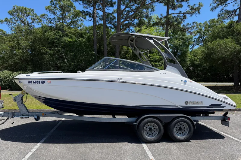 The Image of 2020 Yamaha Boats 212S on trailer, parked outdoors with trees in background. - 1