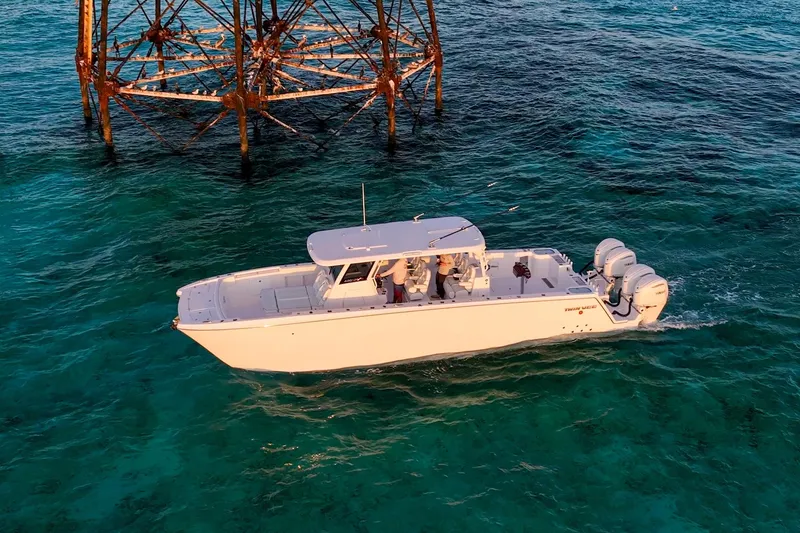 Slide: The Image of 2026 Twin Vee 400 GFX2 CC boat cruising in clear turquoise waters near a metal structure. - 4